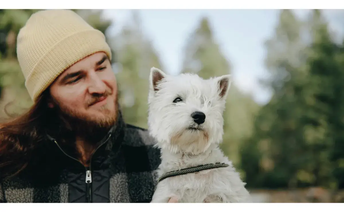 Hombre cargando a un perro blanco. Foto: Pexels/PNW Production