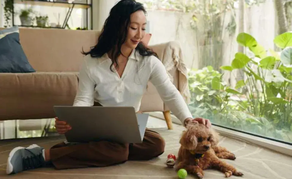 Mujer acariciando a su perro mientras trabaja. Foto: Envato/DragonImages